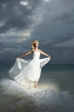Gorgeous bride standing and posing under threatening clouds at sunset. Stock Photos
