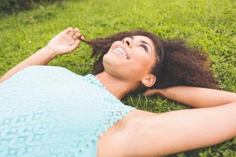 Gorgeous cheerful brunette lying on grass holding lock of hair Stock Photos
