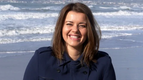 Gorgeous lady smiling happy in front of the ocean in winter at sunset slow mo Stock Footage 115499860