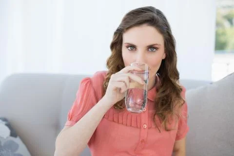Gorgeous pregnant woman drinking glass of water sitting in living room Stock Photos
