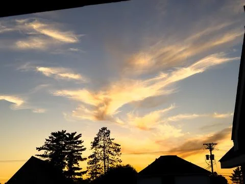 Gorgeous sunset with trees and clouds over the silhouetted small town Stock Photos