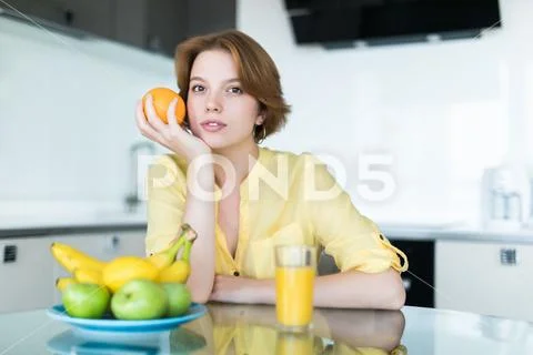 Gorgeous woman drinking a glass of orange juice standing in her kitchen looki Stock Photos