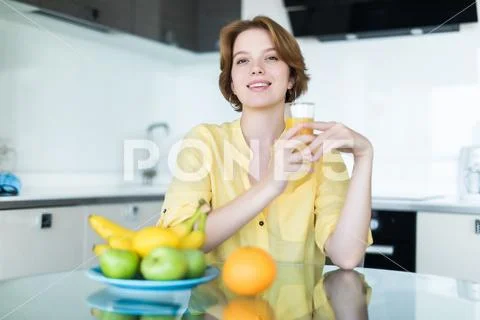 Gorgeous woman drinking a glass of orange juice standing in her kitchen looki Stock Photos
