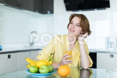 Gorgeous woman drinking a glass of orange juice standing in her kitchen looki Stock Photos