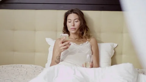 Gorgeous woman using cellphone while drinking champagne in bed Stock Footage 83528734