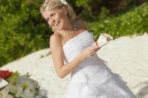 Gorgerous bride smiling, standing in front of table with piece of cake. Stock Photos