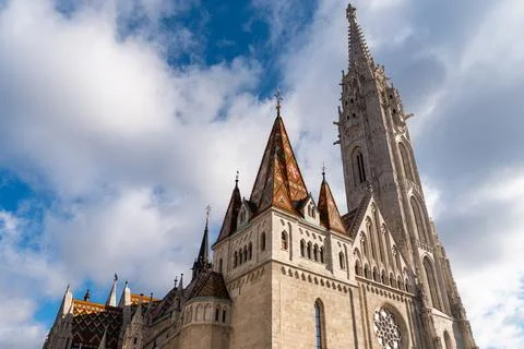 Gothic church tower with patterned tile roof under cloudy blue sky Stock Photos