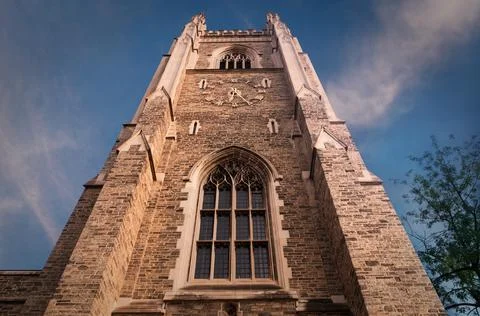 Gothic tower lit with warm sunset rays in front of deep blue sky with white pink Stock Photos