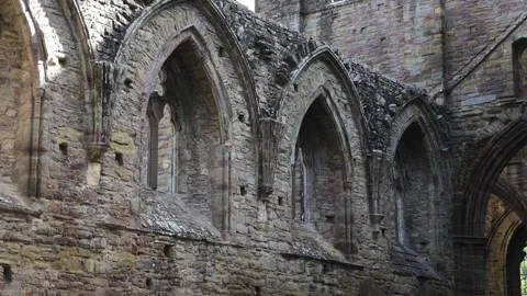 Gothic window arcades of Tintern Abbey church nave fill the frame as the camera Stock Footage 345884695