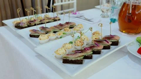 Gourmet appetizer featuring herring mini sandwiches, garnished with cucumber and Stock Photos