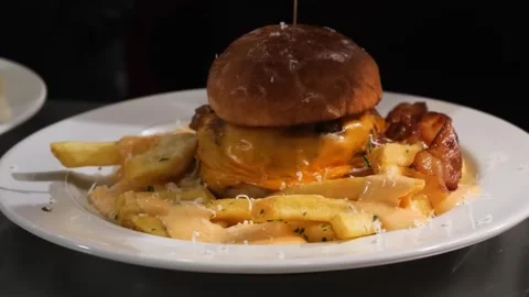 Gourmet Beef Cheeseburger with Molten Cheese and Loaded Fries on White Plate Stock Footage 331633370