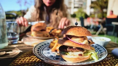 Gourmet burger served on a patterned plate in bright daylight, with blurred Stock Footage 323013260