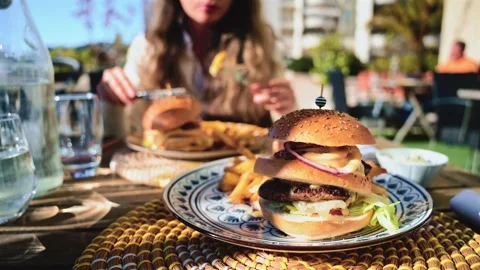 Gourmet burger served on a patterned plate in bright daylight, with blurred Stock Footage 323013741