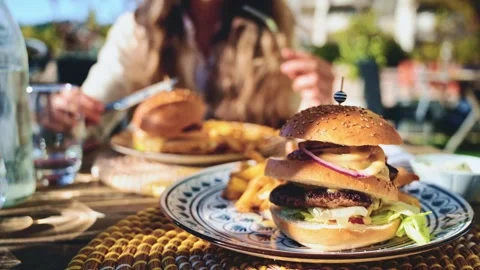 Gourmet burger served on a patterned plate in bright daylight, with blurred Stock Footage 323014368