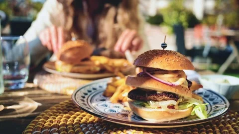 Gourmet burger served on a patterned plate in bright daylight, with blurred Stock Footage 323014571