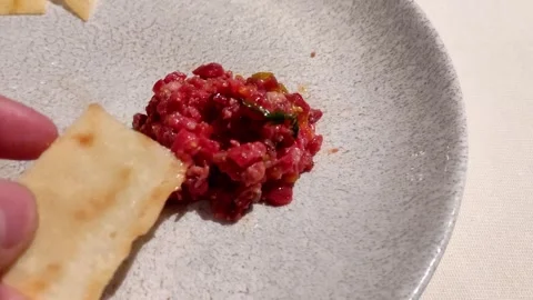 Gourmet dining experience. Hand with cracker picking up steak tartar Stock Footage 242035999
