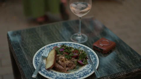 Gourmet dinner plate with roasted meat, salad and wine glass on outdoor table Stock Footage 345268608