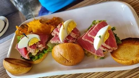 A gourmet dish featuring three small sandwiches topped with seared tuna, le.. Stock Photos