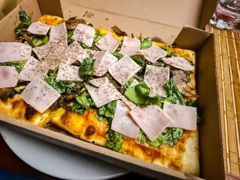 Gourmet rectangular pizza with ham mushrooms and fresh lettuce in cardboard b Foto stock