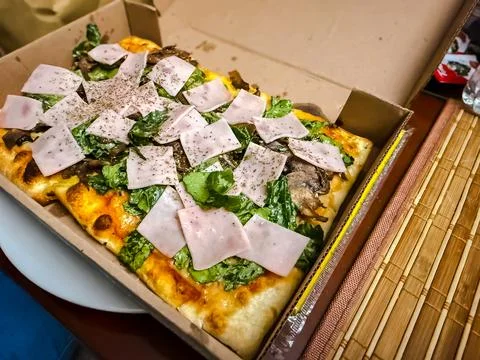 Gourmet rectangular pizza with ham mushrooms and fresh lettuce in cardboard b Stock Photos