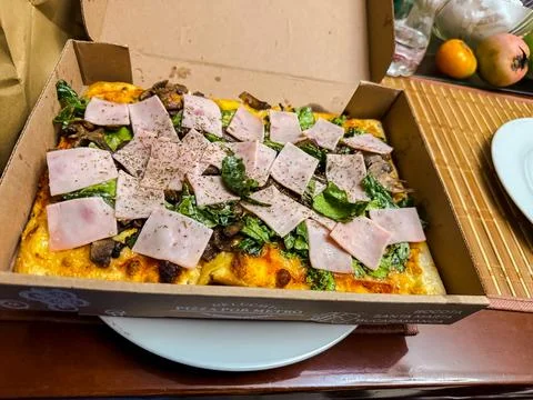 Gourmet rectangular pizza with ham mushrooms and fresh lettuce in cardboard b Stock Photos