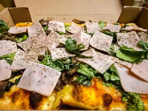 Gourmet rectangular pizza with ham mushrooms and fresh lettuce in cardboard b Stock Photos