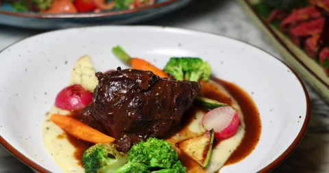 Gourmet slow-cooked beef surrounded by vibrant vegetables and creamy Stock Footage 318118878