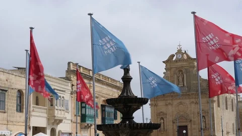 Gozo,Malta-Slow Motion of waving flags around a fountain in the evening Stock Footage 89188235