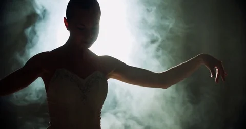 A graceful ballerina dancing ballet elements in the dark with light and smoke on Stock Footage 73423682