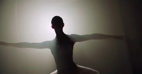 A graceful ballerina dancing ballet elements in the dark with light and smoke on Stock Footage