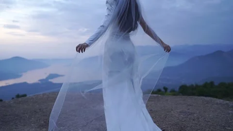 Graceful bride dances on mountain crest during sunrise with flowing veil Stock Footage 343167820
