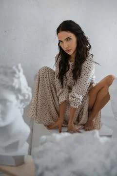 Graceful brunette model in dress amidst Greek sculptures in an artist's studio Stock Photos