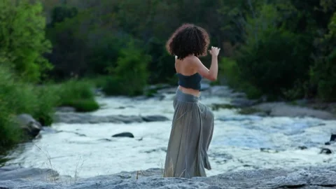 A graceful dancer poses by a serene river, capturing the essence of nature and Stock Footage 318919761