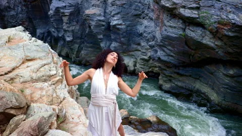 A Graceful Performance by a Dancer on a Rocky Riverbank Amidst a Scenic Stock Footage 314056575