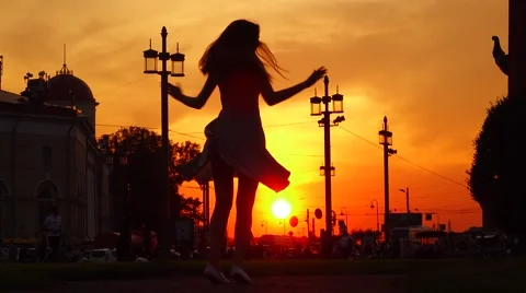 Graceful woman in flying skirt spin around against golden sunset, silhouette Stock Footage