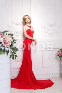 Graceful young adult woman, with red long dress, jewelry and blonde wavy hair Stock Photos