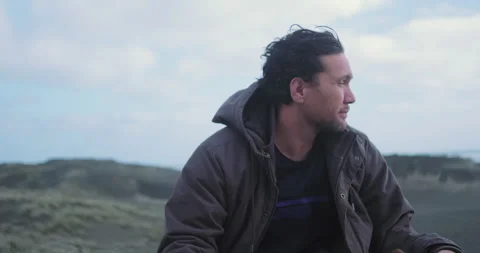Graded C4K 120fps Man sitting on sand dune looking out to sea Stock Footage 136561495