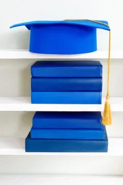 Graduation blue mortarboard on top of stack of books on wooden shelf Stock Photos