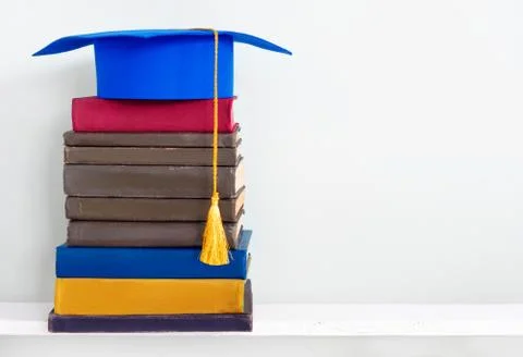 Graduation blue mortarboard on top of stack of books on wooden shelf 스톡 사진