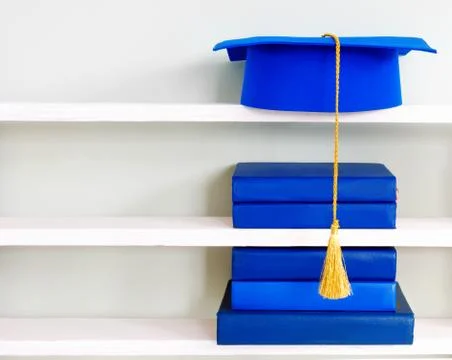 Graduation blue mortarboard on top of stack of books on wooden shelf on backg Stock Photos