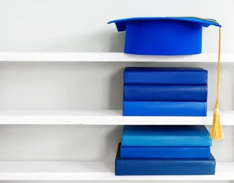 Graduation blue mortarboard on top of stack of books on wooden shelf Stock Photos
