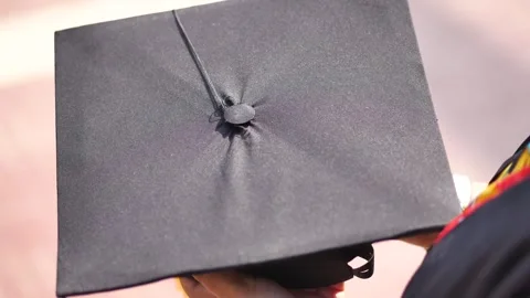 Graduation cap held by student in black gown during outdoor commencement ce.. Stockbeeldmateriaal 332579232