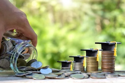 Graduation cap on a stack of coins that runs out of a money jar. Money saving Stock-Fotos