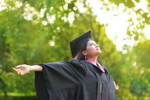 Graduation day Young Asian Indian female student open arms outdoor on grad... Stock Photos