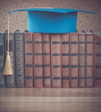 Graduation mortarboard on top of stack of books on a wooden table on backgrou Stock Photos