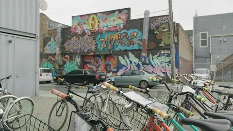 GRAFFITI ON A CITY WALL PAN DOWN TO ROW OF BICYCLES PARKED UP Stock Footage 127470756