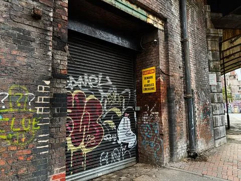 Graffiti covered brick wall and shuttered storefront in Manchester UK alleywa Stock Photos