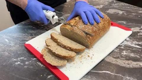 Grainy brown loaf of bread being sliced with electric knife Stock Footage 311726444