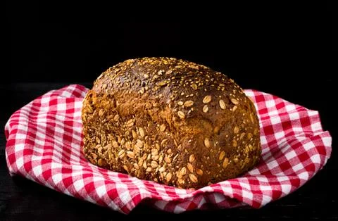 Granary spelt bread on red kitchen towel and black background Stock Photos