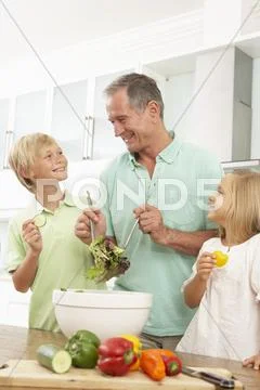 Grandchildren Helping Grandfather To Prepare Salad In Modern Kitchen Stock-Fotos
